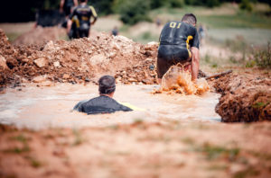 Extreme cross country runners moving through dirty puddle, mud obstacle